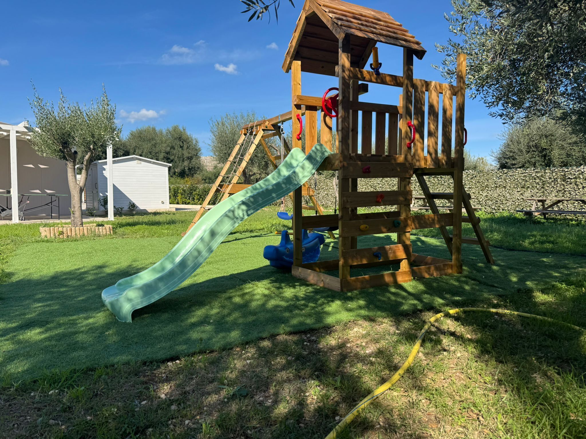 A wooden play structure with a slide, climbing wall, and a small roofed shelter.