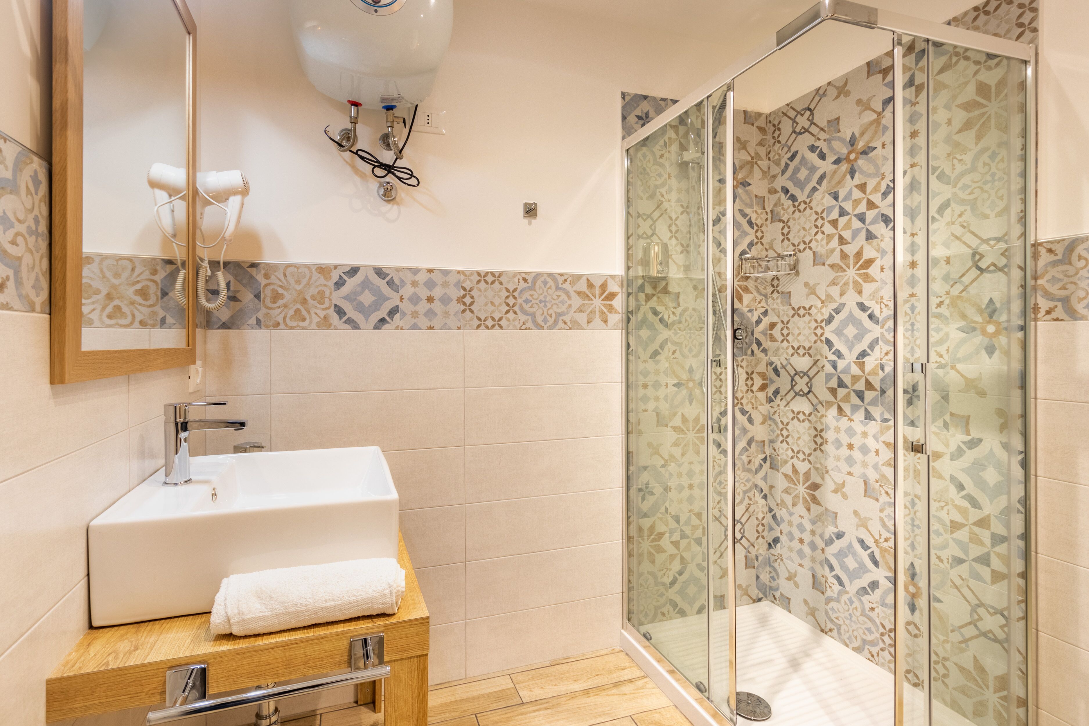 Un baño moderno con un lavabo grande de color blanco, una ducha con mampara de vidrio y azulejos con diseño.