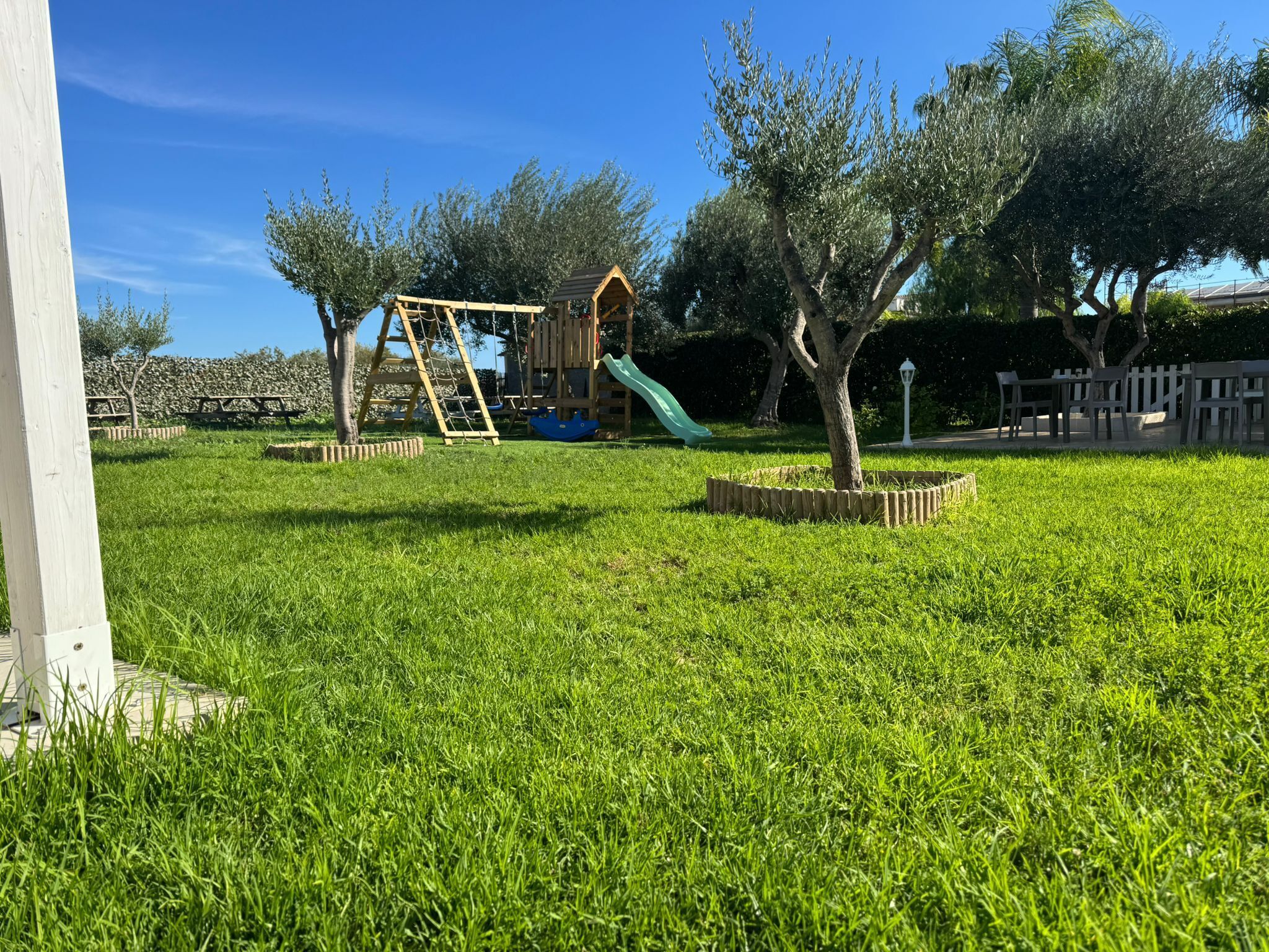 A grassy playground area with a wooden play structure and a slide.