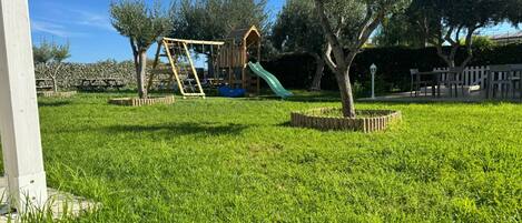 A grassy playground area with a wooden play structure and a slide.