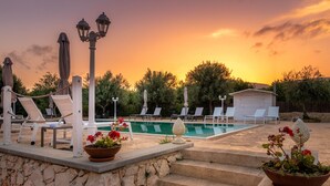A poolside area with lounge chairs, a stone wall, and a small shed. - Tramonto Ibleo Resort (Avola)