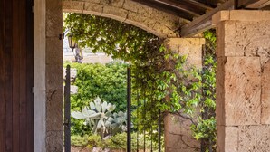An arched stone doorway with a metal gate, leading to a garden area with cacti and greenery. - Tramonto Ibleo Resort (Avola)