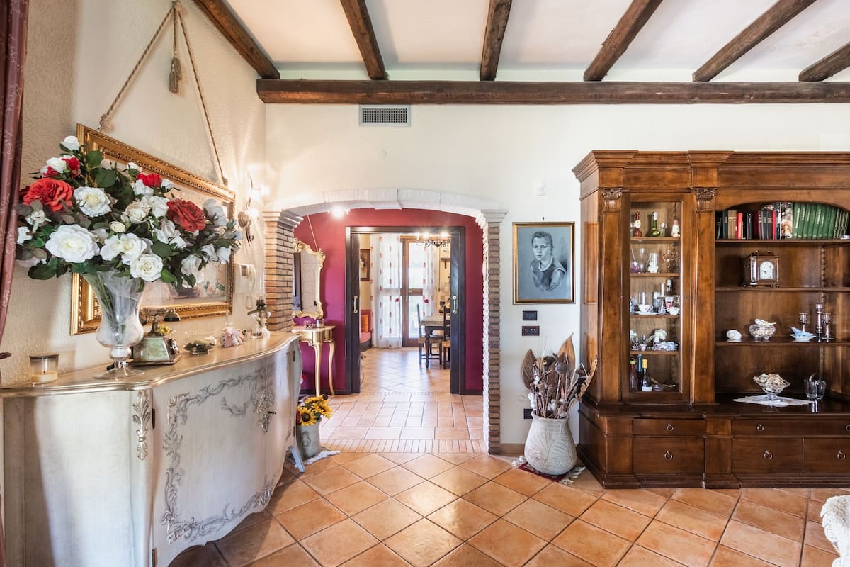 A spacious hallway with a tiled floor, a wooden cabinet with glass doors, and a mirror with a floral arrangement.