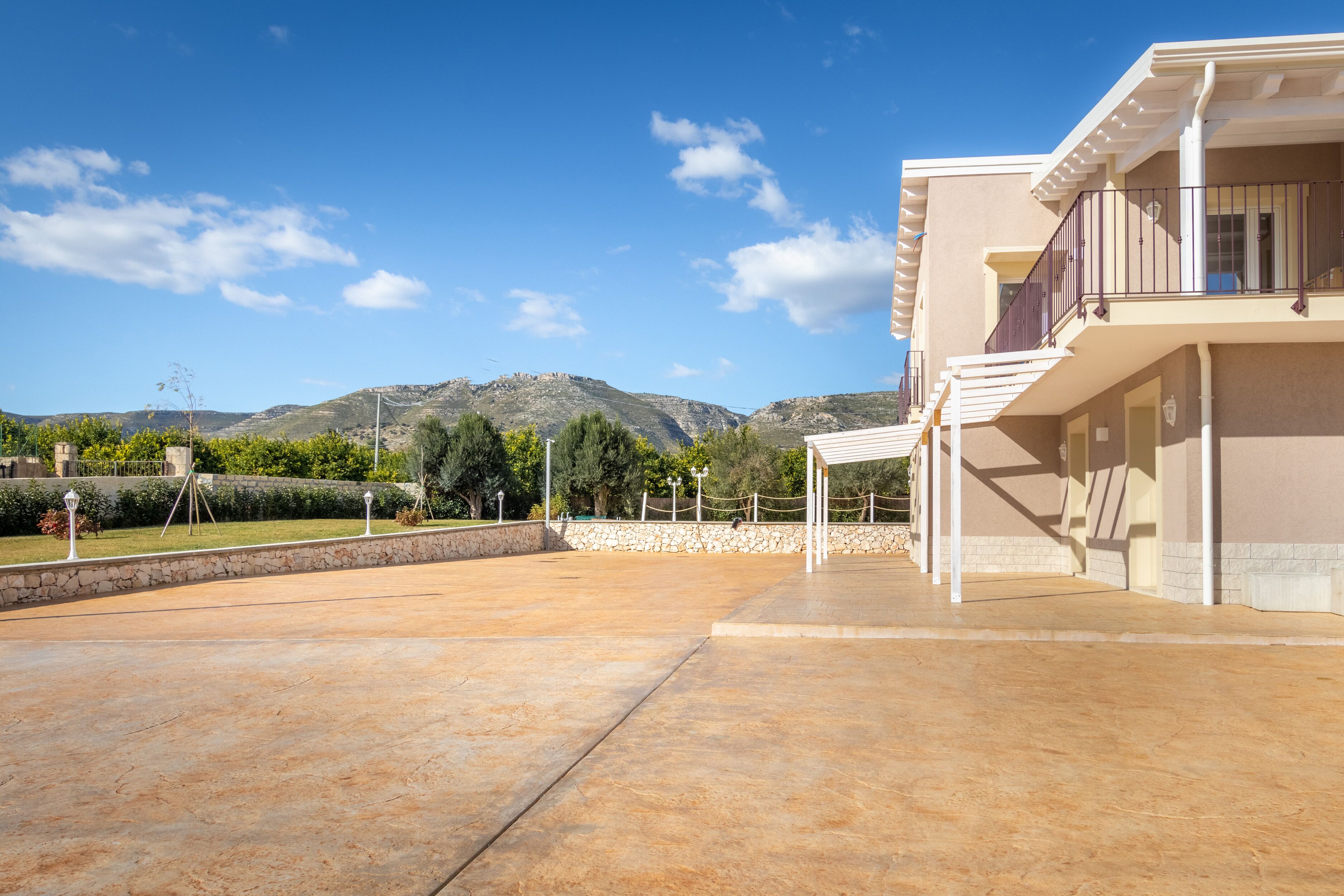 Un edificio moderno con balcón, un patio empedrado y montañas al fondo.