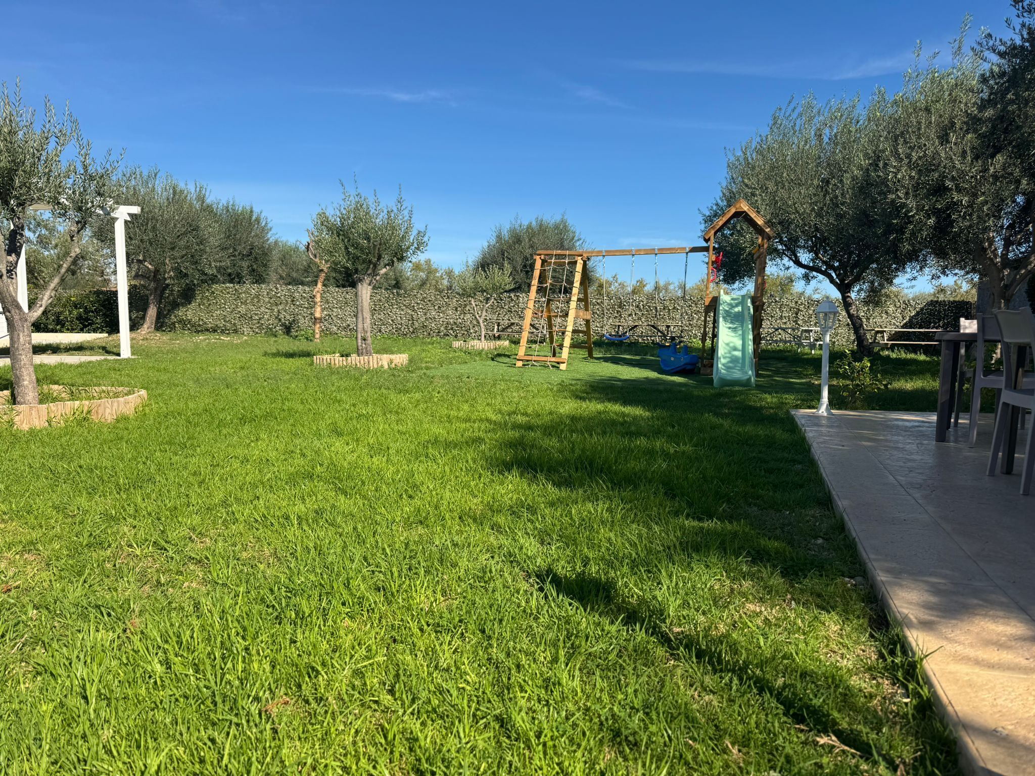 A well-maintained grassy area with a swing set, a small play structure, and a bench.