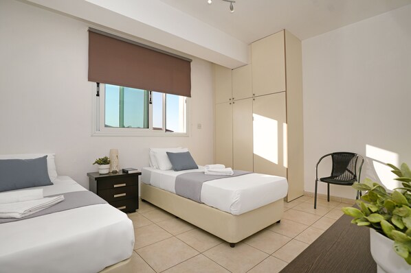 Un dormitorio moderno con dos camas, una mesita de noche, una silla y un ventanal con vistas.