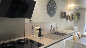 Een moderne keuken met een flatscreen televisie, waterkoker, spoelbak en een wandklok.