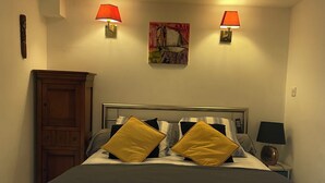 Een net opgemaakt bed met gestreepte lakens, twee bedlampjes, een houten kast en een schilderij aan de muur.