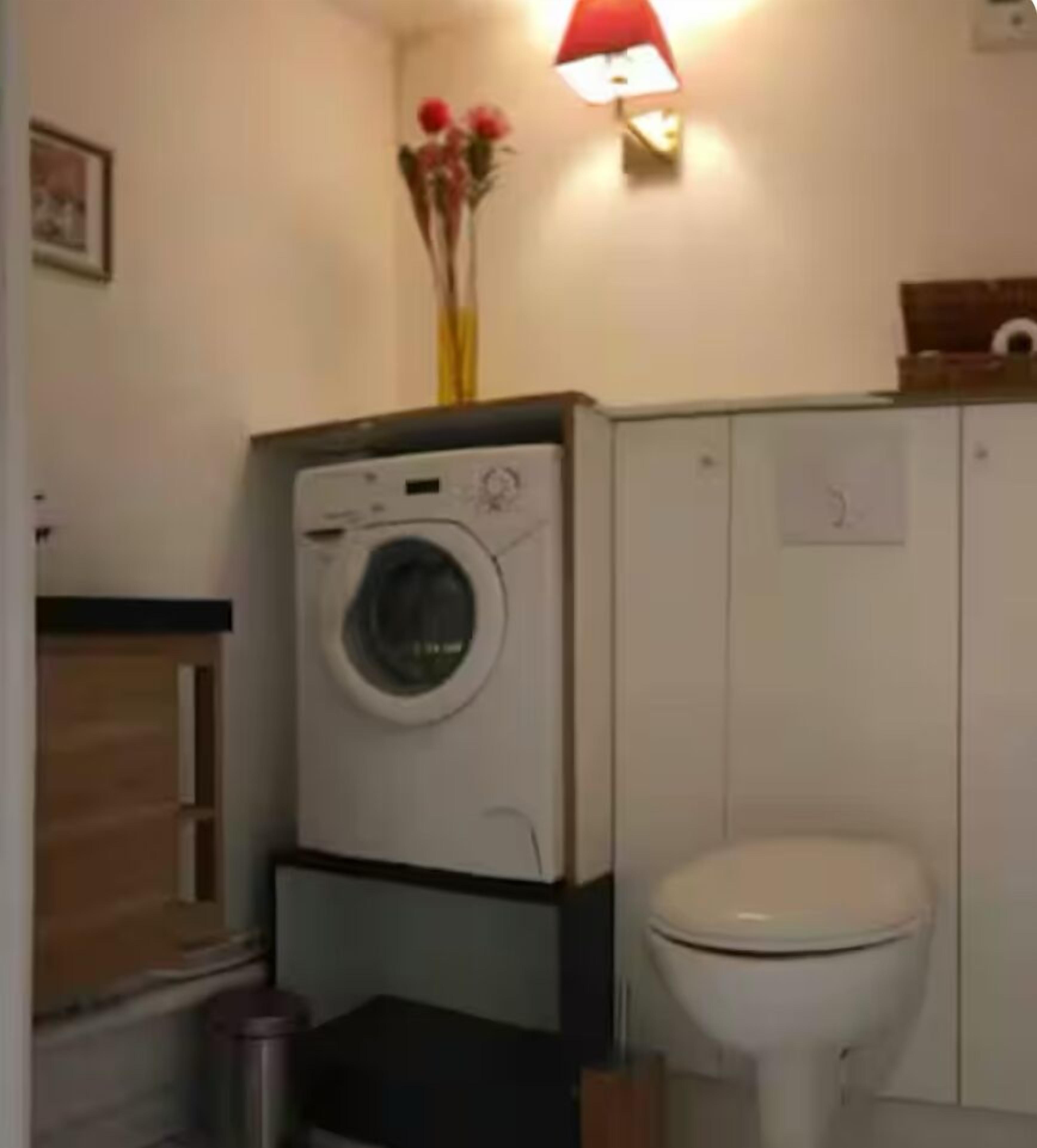 A compact bathroom with a washing machine, toilet, and a small trash bin.