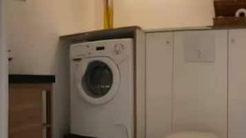 A compact bathroom with a washing machine, toilet, and a small trash bin.