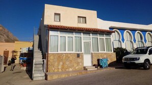 A two-story building with a stone facade, a flat roof, and a blue and white mural on the side. - House near the bay of Cornino (Cornino)