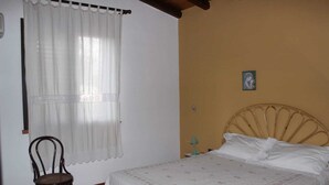 A bedroom with a bed, a chair, a window with curtains, and a wall-mounted lamp. - House near the bay of Cornino (Cornino)