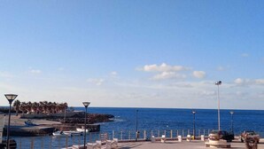 A coastal promenade with a clear view of the sea, a row of white benches, and a few boats docked at the pier. - House near the bay of Cornino (Cornino)