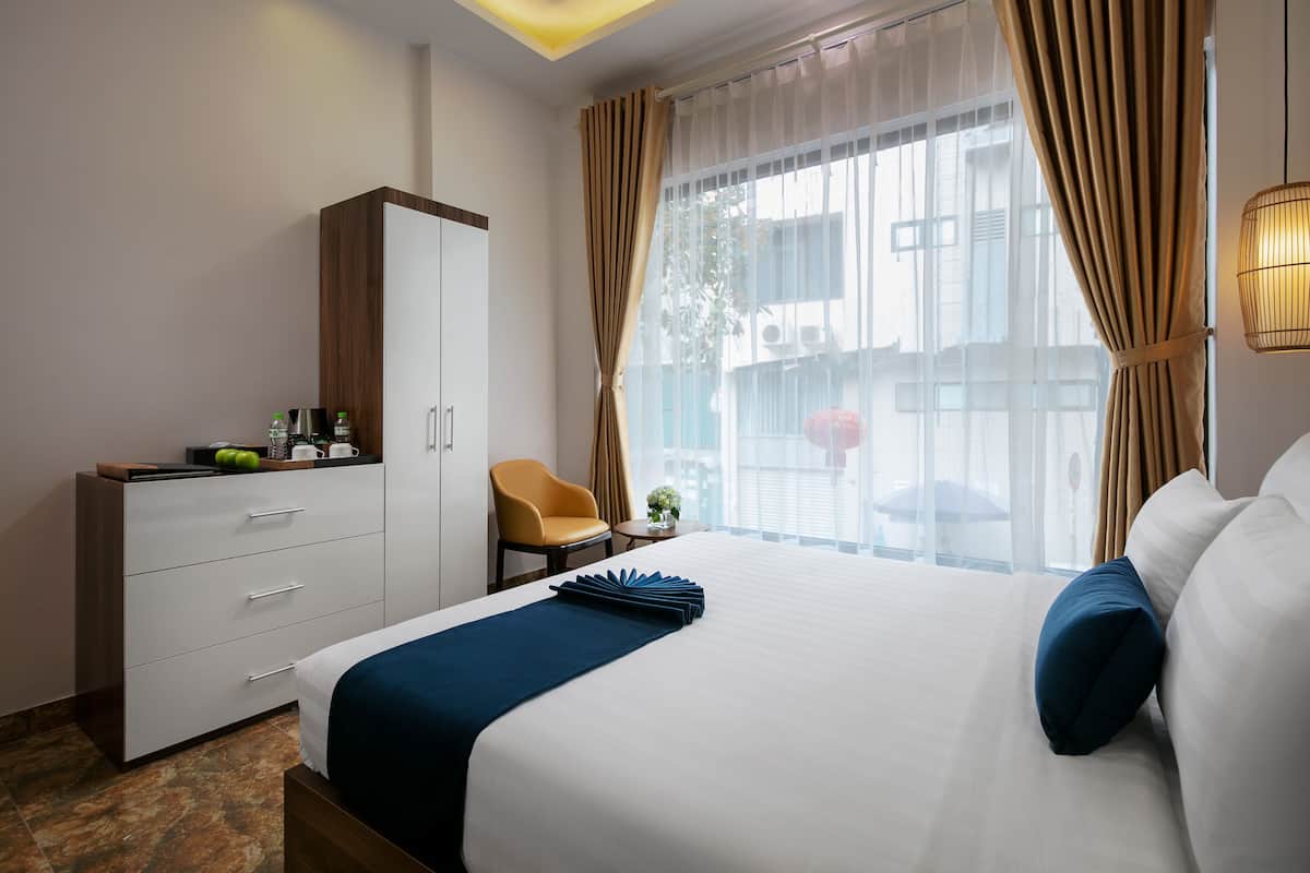 A hotel room with a large bed, a wardrobe, a chair, and a small table with a plant.