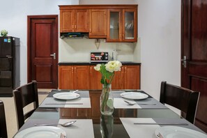 Un coin repas avec une table en verre, deux chaises et un vase rempli de fleurs blanches. On aperçoit en arrière-plan des meubles en bois et un four à micro-ondes.