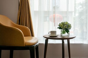 Una habitación con un sillón de cuero, una mesita redonda con una taza blanca y un florero, y cortinas traslúcidas.