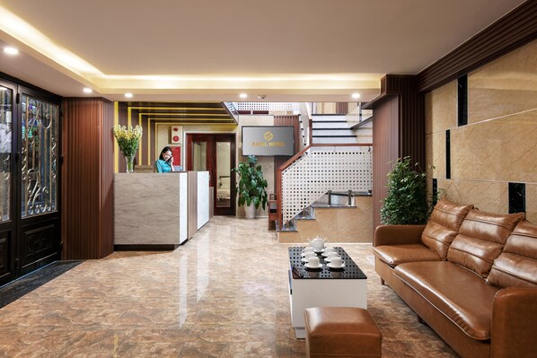 Un hall de hotel con mostrador de recepción, una escalera, un sofá de cuero y una mesa de centro.