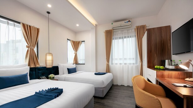 Hotellihuone, jossa on kaksi sänkyä, työpöytä, tuoli, televisio ja ikkuna, jossa on verhot.