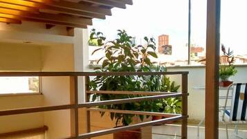 Un interior moderno con barandilla de vidrio, techo de madera y vistas a un balcón con plantas.
