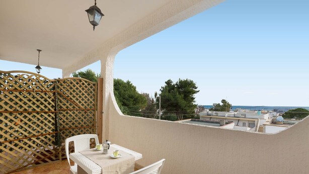 Varanda com mesa e cadeiras, um painel treliçado e vista para edifícios e árvores.