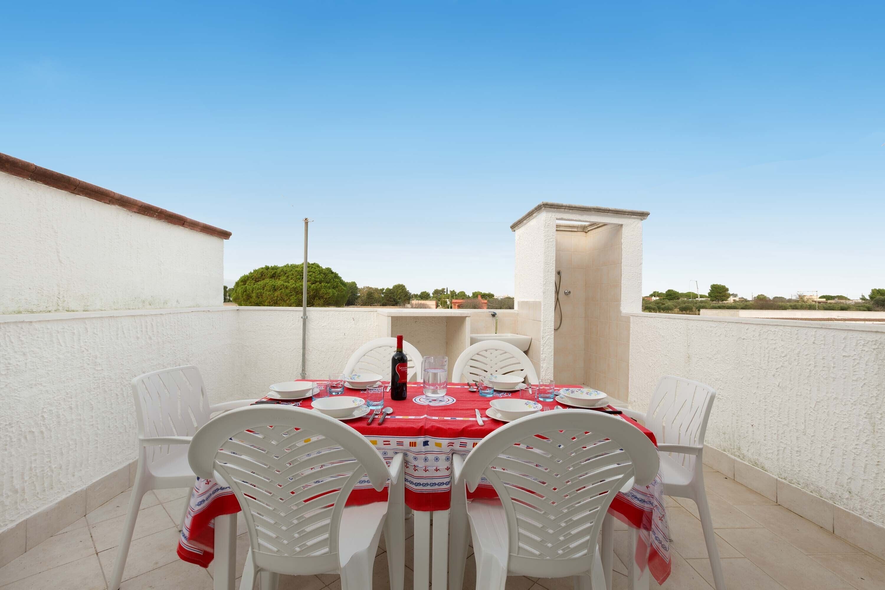 Un patio al aire libre con una mesa dispuesta para cuatro personas, sillas blancas y mantel rojo.