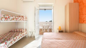 Quarto com uma cama beliche, uma cama de solteiro, uma mesinha e uma cadeira.