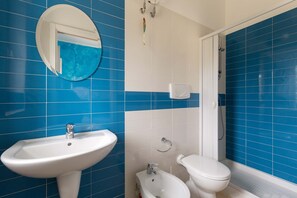 Um banheiro com paredes azulejadas em azul, pia branca, vaso sanitário e bidê.