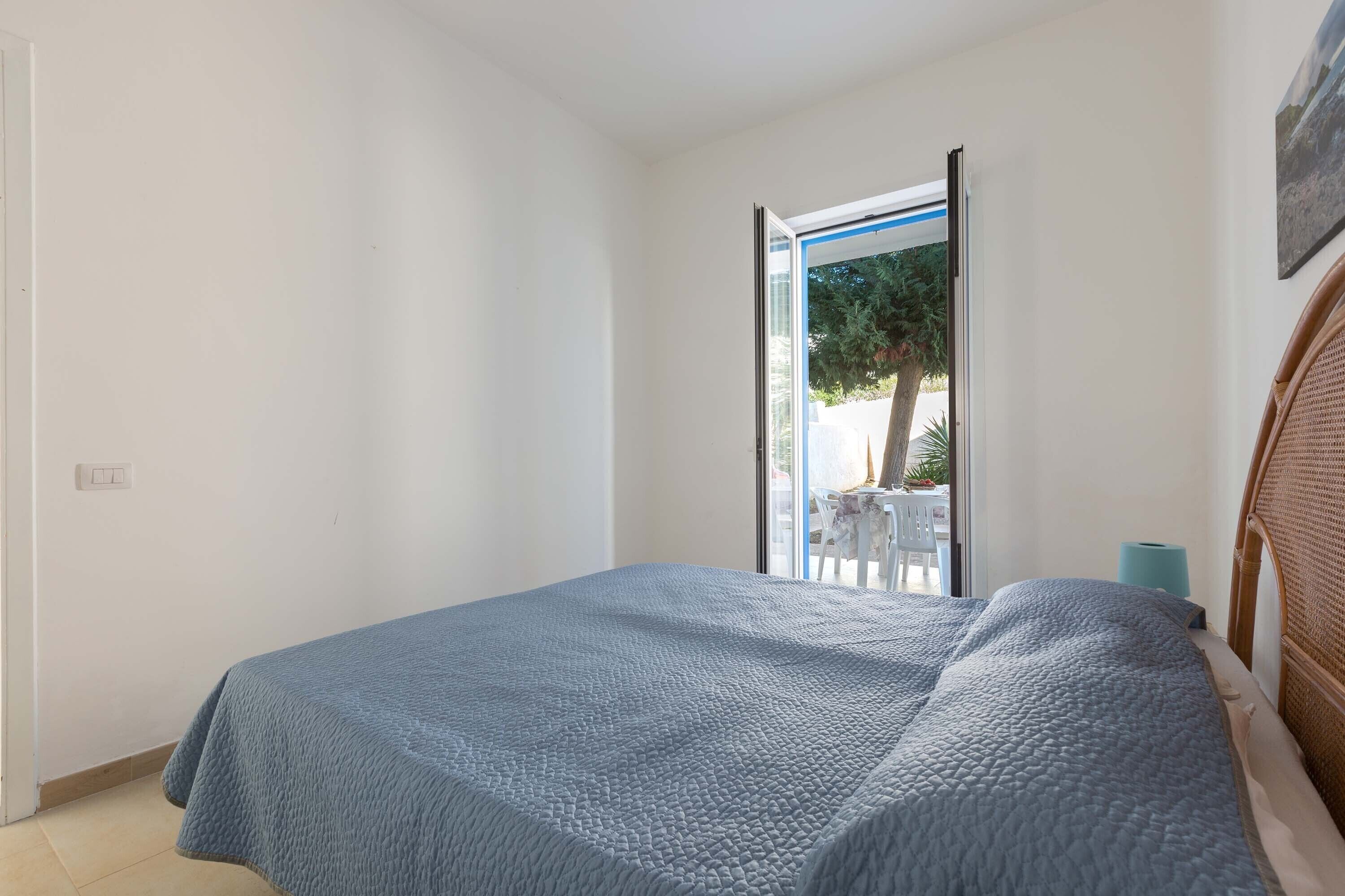 Une chambre à coucher avec un lit, une porte et une vue sur un espace extérieur aménagé avec une table et des chaises.