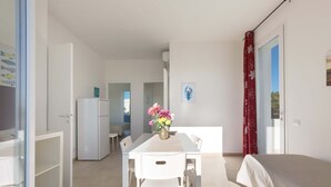Een moderne, goed verlichte kamer met een eettafel, stoelen, een koelkast en een bed.