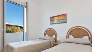Een kamer met twee bedden, een schilderij van een zonsondergang en uitzicht op het omliggende landschap.
