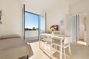 Une chambre moderne avec un lit, une table à manger et des chaises, un vase de fleurs et une vue à travers une porte vitrée.