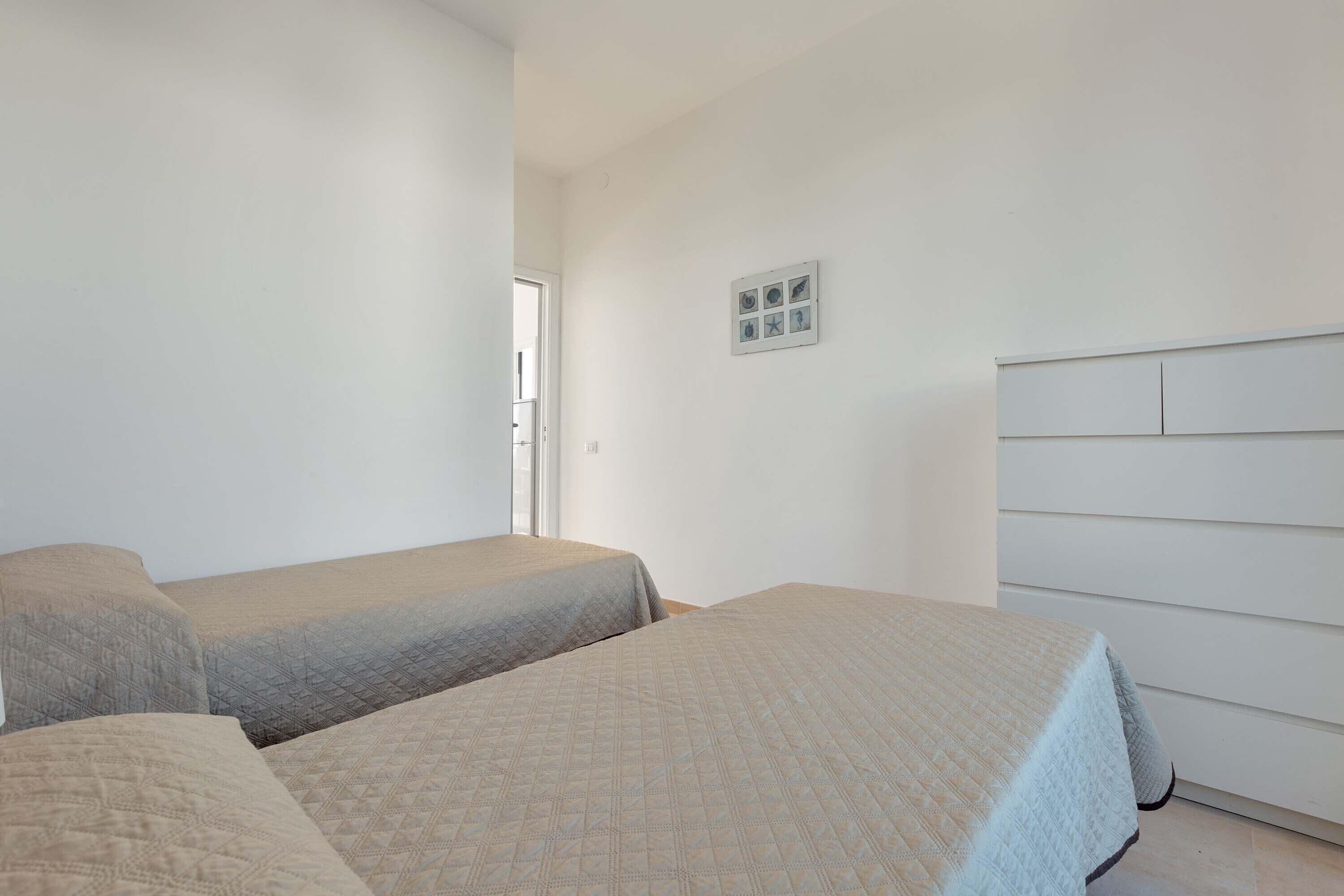 A bedroom with two beds, a white dresser, and a small wall-mounted shelf with decorative items.