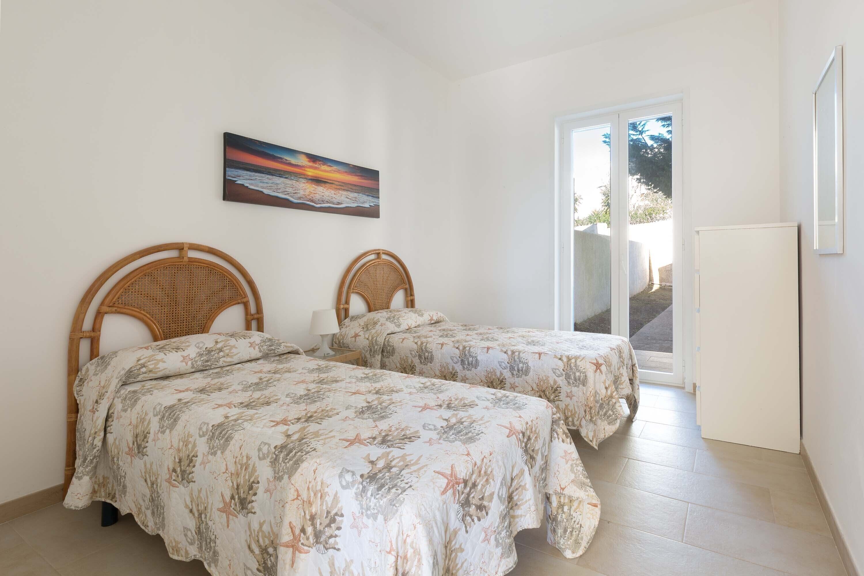 A room with two beds, a painting of a sunset, and a door leading to an outdoor area.