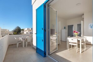 A balcony with a blue door, white chairs, and a table with a vase of flowers.