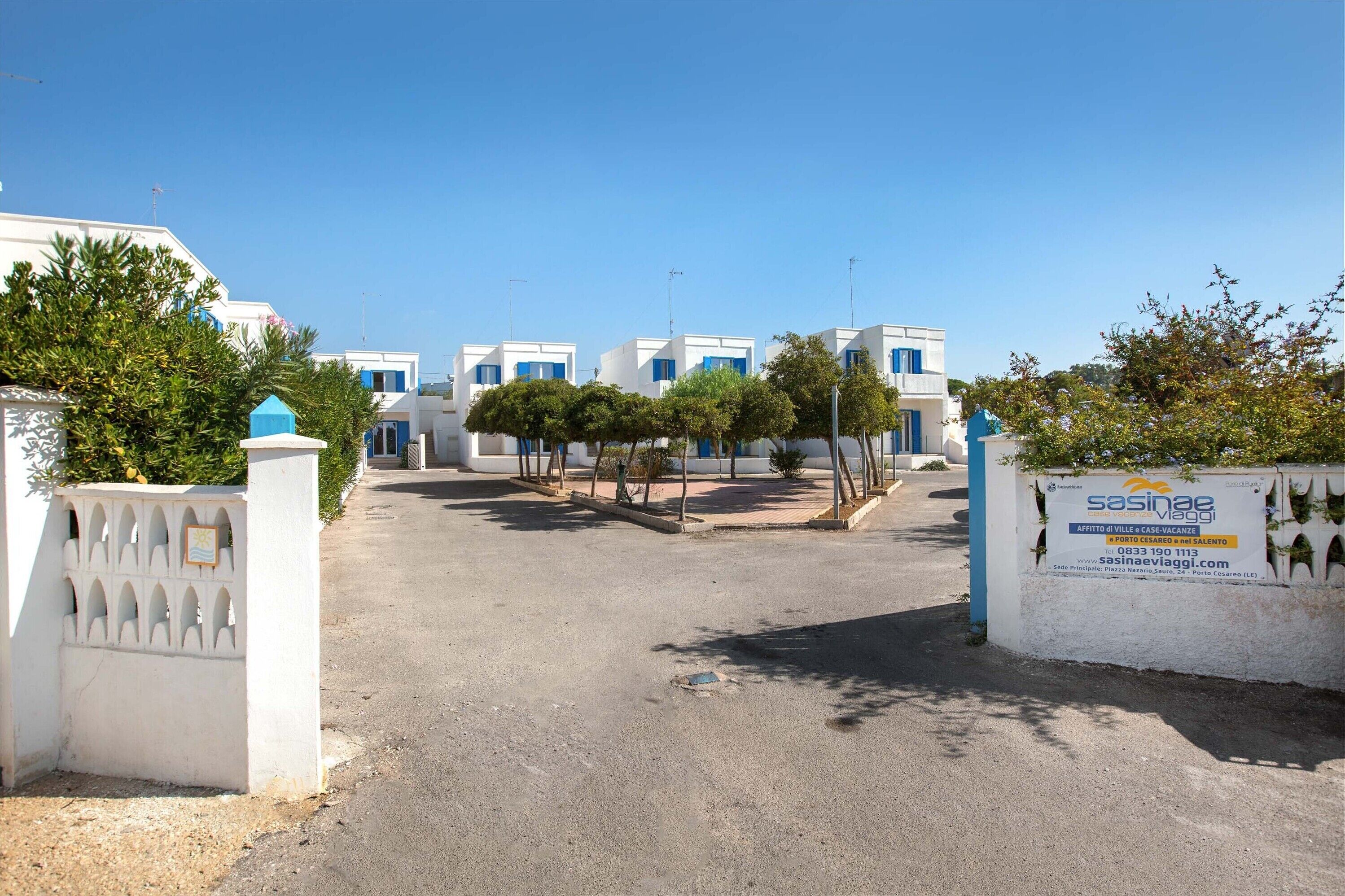 A row of white buildings with blue doors, a paved entrance, and a signboard.