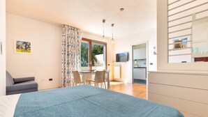 Ein Schlafzimmer mit Bett, Schreibtisch und Stuhl. Es gibt ein Fenster mit Vorhängen, einen Fernseher und eine Heizung.