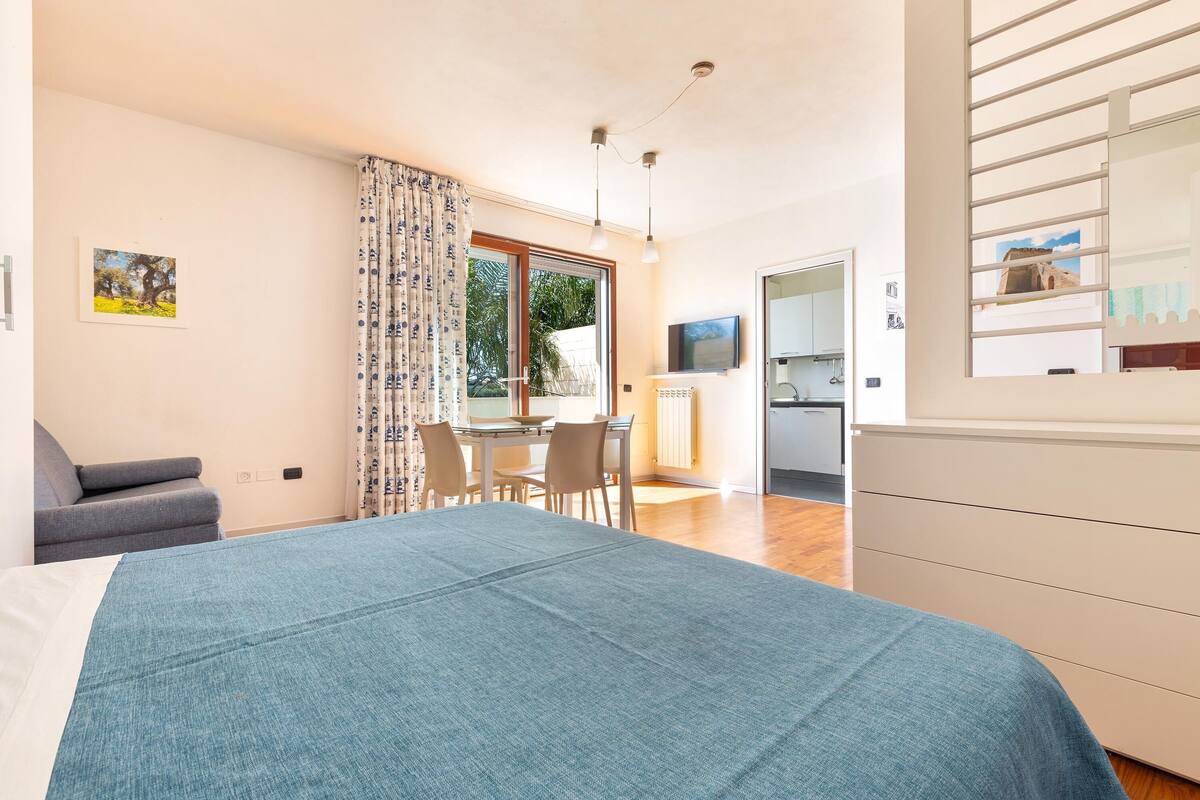 Een slaapkamer met een bed, een bureau en een stoel. Er is een raam met gordijnen, een televisie en een radiator.