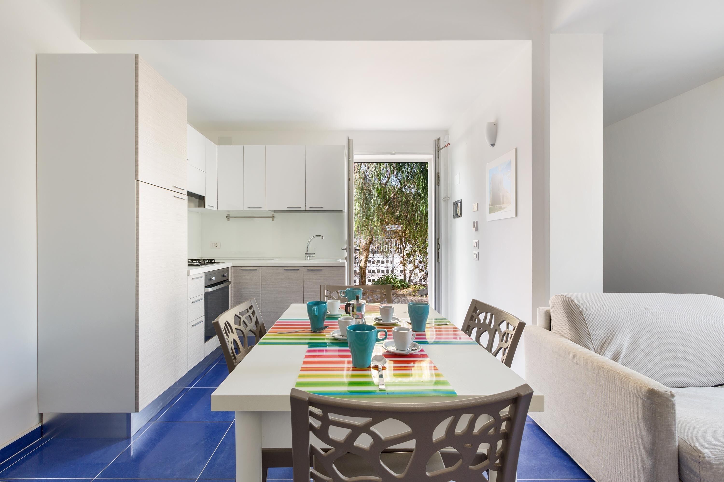 A modern kitchen with white cabinets, a dining table with chairs, and a view of the outdoors.