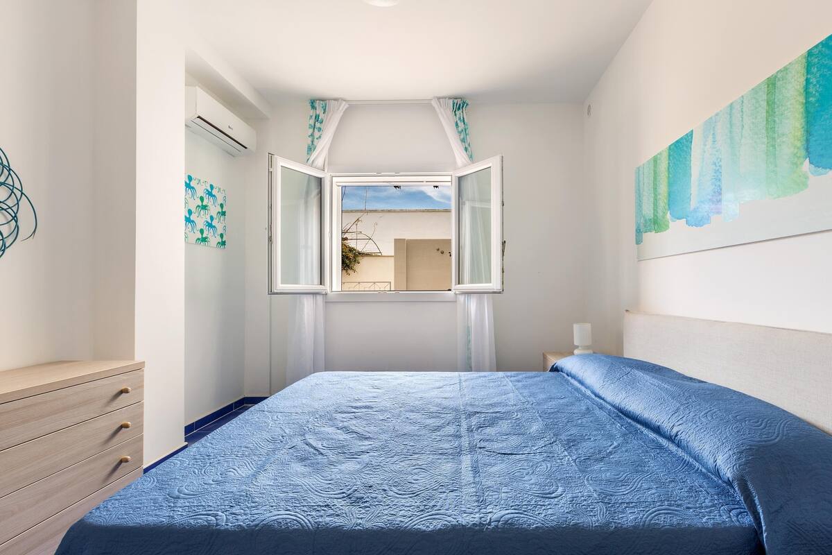 A bedroom with a bed, a dresser, and a window with curtains.