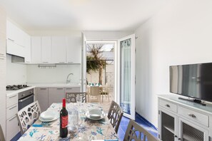 A modern kitchen with white cabinets, a dining table set with plates, a bottle of wine, and a TV on a cabinet. - Residence Spiaggia d'Oro (Porto Cesareo)
