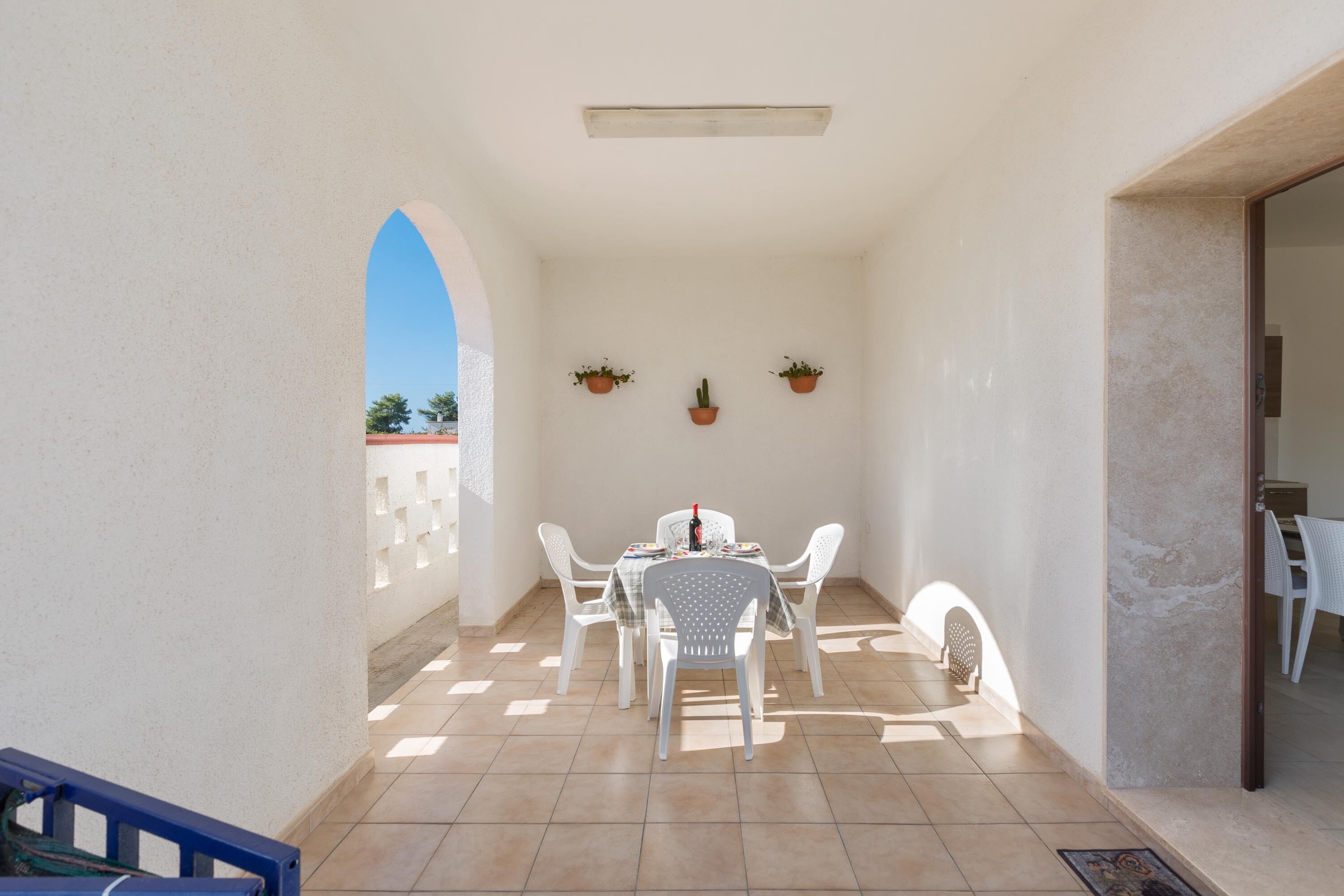 A sunlit patio with a table and chairs, potted plants, and a view of the sky.