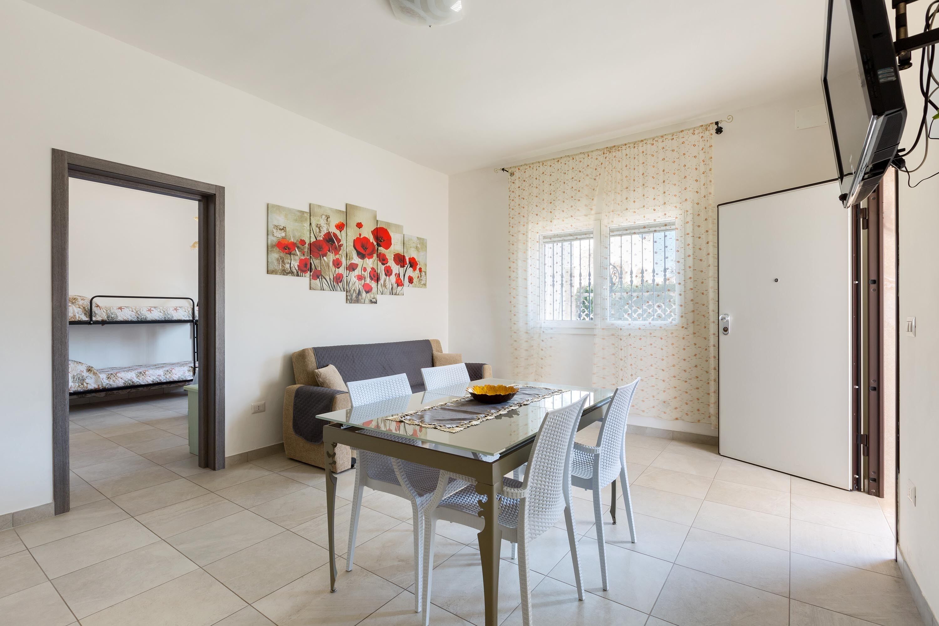 Un espace de vie compact comprenant un coin repas, un canapé, un lit superposé et une fenêtre avec des rideaux.