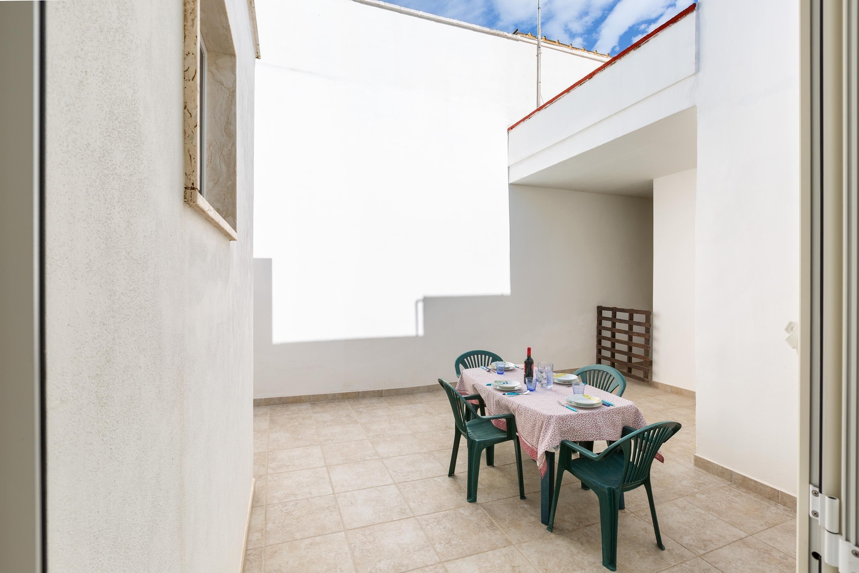 A small patio with a table set for two, chairs, and a view of the sky.