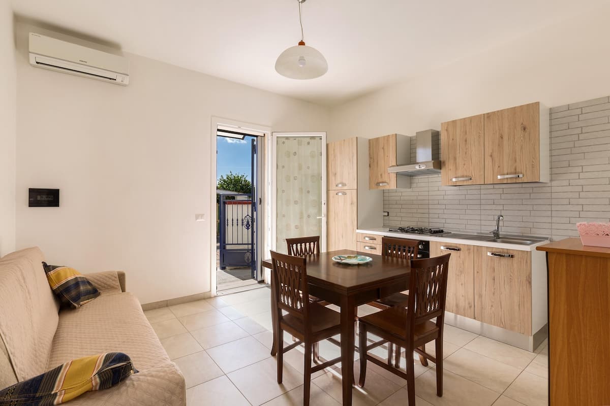 Un espace de vie compact comprenant un coin repas, une kitchenette et un canapé agrémenté de coussins à motifs.