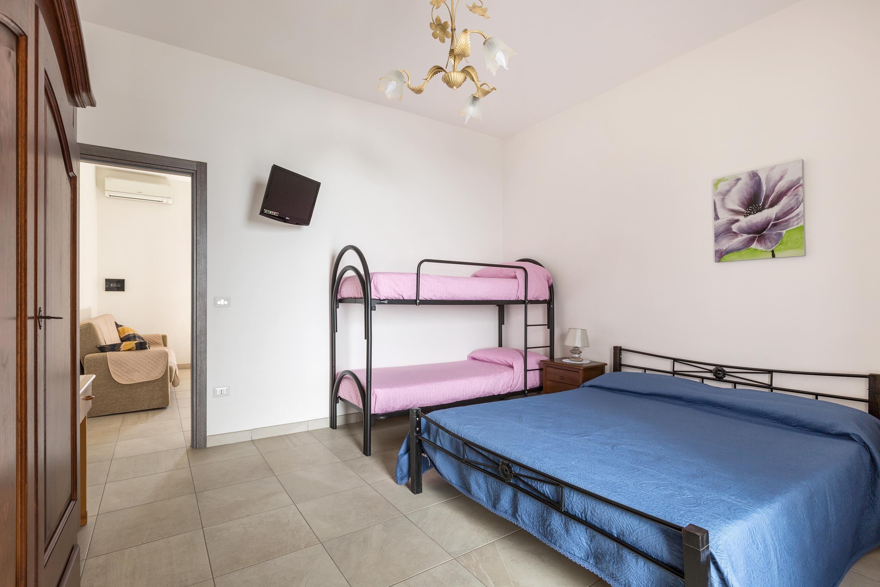 Een kamer met stapelbedden, een flatscreen televisie, een schilderij en een deur naar een andere kamer.