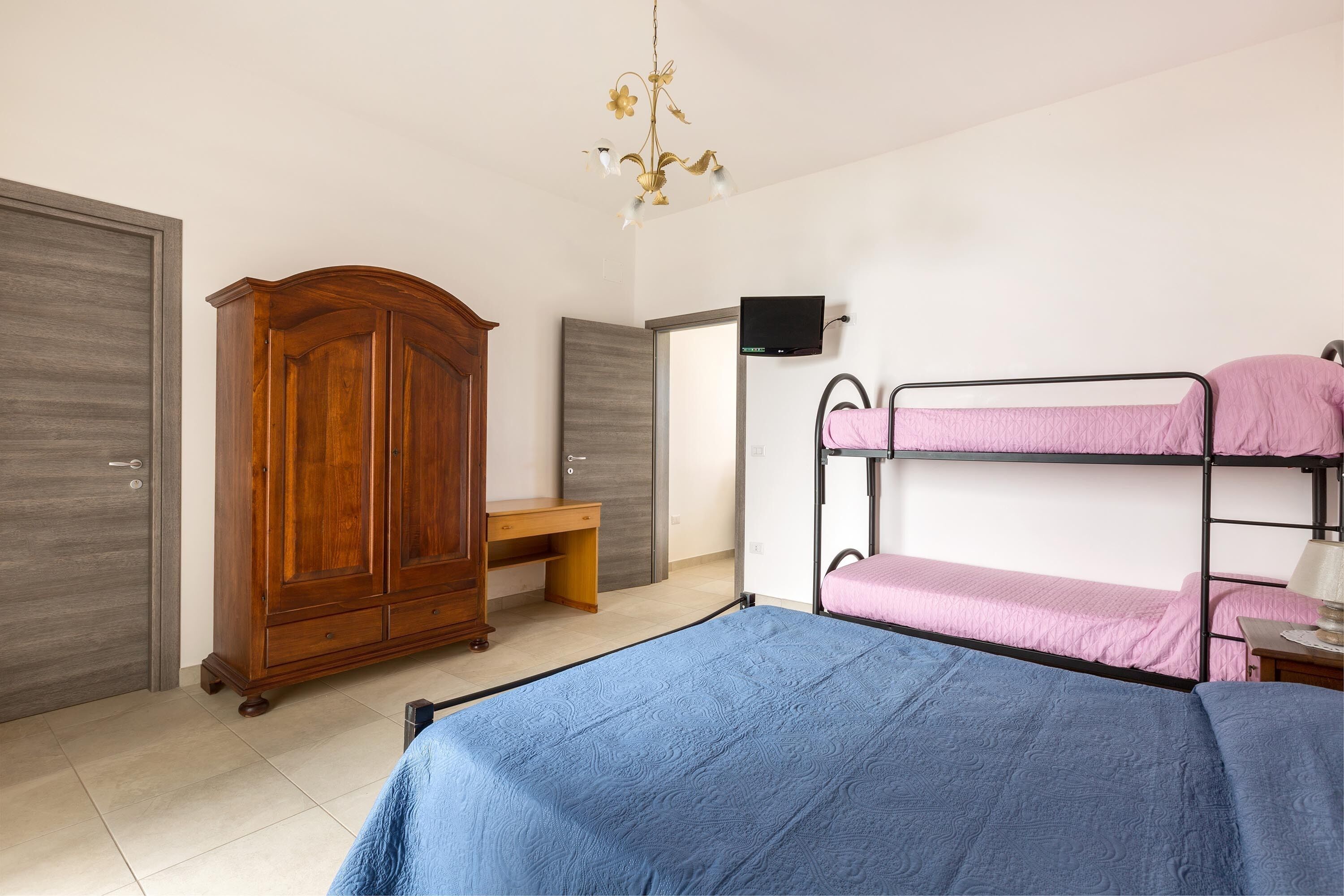 Una camera da letto con una cuccetta, un armadio in legno, una scrivania e un televisore appeso al muro.