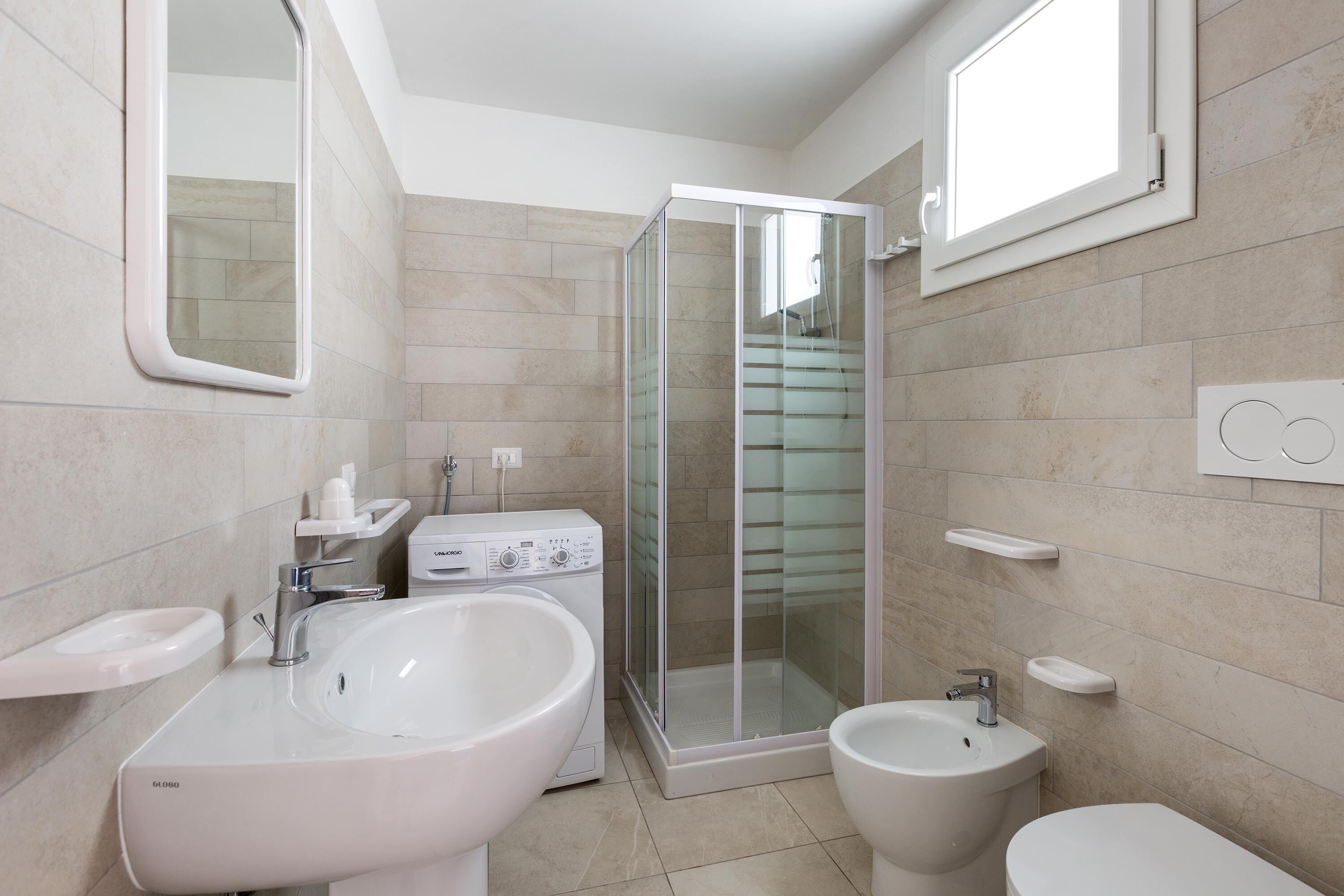 Un baño moderno con ducha envuelta en cristal, un lavamanos grande, un bidé y un inodoro.