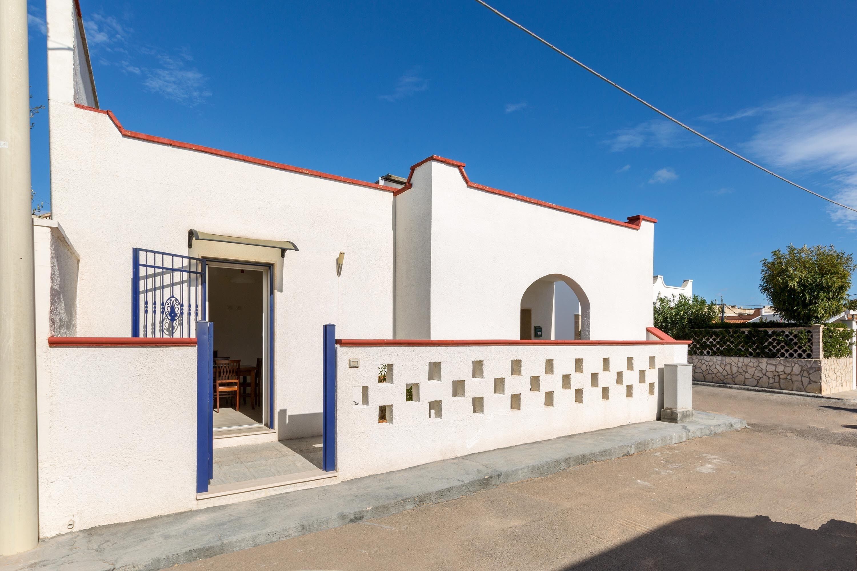 A white building with a red roof, a blue gate, and a stone wall.
