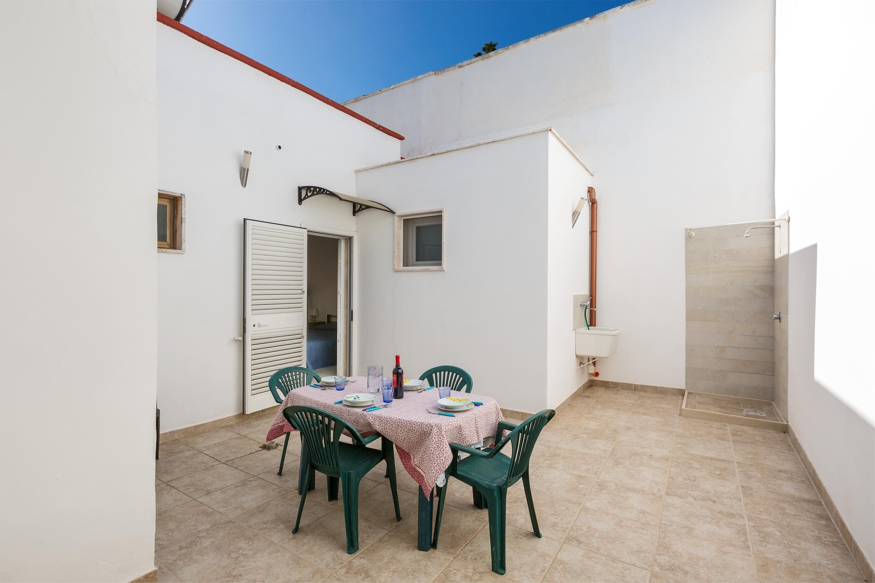 Une petite terrasse extérieure avec une table et des chaises, une porte et un espace douche.