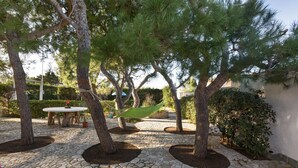 A stone-paved patio with trees, a hammock, and a round table with chairs. - Villetta Spiaggia Bella (Lecce)